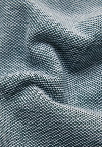 Teksturowana tkanina z zielonym i białym wzorem tkanego materiału, cechująca się gęstym splotem i miękką powierzchnią, prezentująca lekkie fałdy i zmarszczki.