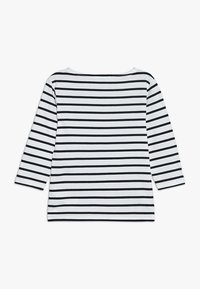 Haut à manches longues rayé avec un motif noir et blanc. Dispose d'un col rond et d'une texture douce avec des manches trois-quarts.