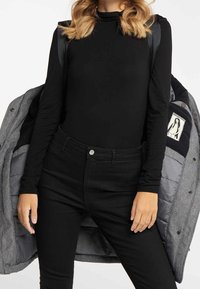 Haut noir à manches longues associé à un jean noir taille haute, rehaussé d'une doudoune grise avec une doublure matelassée et un détail graphique.