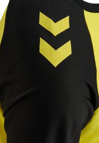 Gros plan d'un maillot de sport noir et jaune avec deux chevrons jaunes pointant vers le bas sur la poitrine.