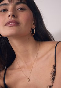 Close-up of a woman wearing gold hoop earrings, a delicate gold necklace with small pendants, and a black lace-trimmed thin strap top.