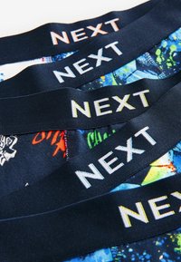Quatre ceintures bleu foncé avec le mot NEXT en lettres blanches et colorées sur un tissu à motifs en dessous.