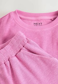 Rosa ribbet stof bluse med rund halsudskæring, parret med matchende ribbet shorts med elastisk talje.