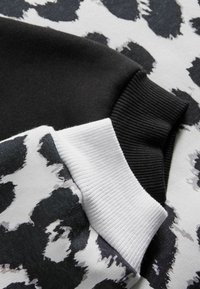 Polsino di felpa nera accanto a un polsino bianco con una stampa animale bianca e nera. Tessuto di cotone morbido con dettagli in texture a costine.