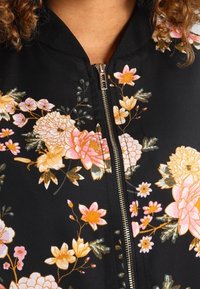 Czarna kurtka bomber wykonana z tkaniny, zdobiona kwiatowym haftem w kolorach różowym, białym i żółtym. Posiada przedni zamek błyskawiczny i ściągacz przy kołnierzu.