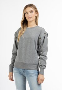 Grijze sweatshirt met een ronde hals, textuurstof, schouderknopen en geribde manchetten en zoom. Gecombineerd met lichtblauwe jeans.