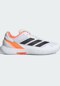 Άσπρο αθλητικό παπούτσι με αναπνεύσιμο πάνω μέρος, πορτοκαλί λεπτομέρειες, τρεις μαύρες ρίγες και υφή στη σόλα σχεδιασμένη για ταχύτητα και σταθερότητα.