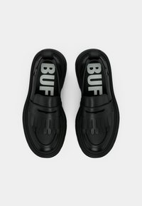 Svarte slip-on sko med en strukturert design med heksagonale detaljer og dristig "BUF"-merke på innersålene. Glatt gummimateriale.