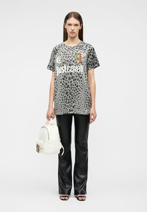 Femme portant un t-shirt Just Cavalli gris à imprimé léopard, un pantalon en cuir noir, des sandales noires, tenant un sac à dos blanc avec un détail floral.