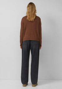 Brauner Strickpullover mit entspanntem Schnitt, geripptem Saum und Nahtdetail auf der Rückseite, kombiniert mit hoch taillierten, dunkelgrauen Hosen mit weitem Bein.