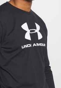 Svart långärmad tröja i mjukt tyg med en stor vit Under Armour-logo på framsidan och en ren design på halsringningen.