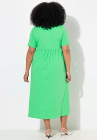 Vihreä, lyhythihainen maksimekko, jossa on kootun vyötärön muotoilu ja sileä rakenne. Yhdistetty hopeisiin korollisiin sandaaleihin.
