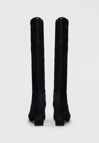 Black suede knee-high boots with a textured finish, block heel, and visible stitching detail, designed for a fitted look.
