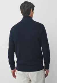 Dunkelblauer Strickpullover mit hohem Kragen. Verfügt über gerippte Bündchen und einen Saum und präsentiert eine glatte Textur sowie ein klassisches Pullover-Design.