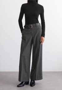 Zwarte geribbelde coltrui gecombineerd met grijze wollen broek met wijde pijpen. Bevat een zwarte riem met een gouden gesp en zwarte hoge hakken met puntige tenen.