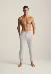 Lys grå joggere lavet af blød, letvægtsstof med elastisk talje, snøre og ribbede mansjetter, båret uden sko.