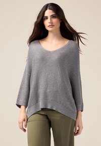 Grauer gestrickter Pullover mit entspanntem Schnitt, geripptem Saum und weiten Ärmeln. Weiche Textur und tiefer V-Ausschnitt, getragen über olivgrünen Hosen.