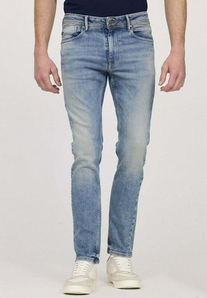 Jean en denim bleu clair avec une coupe ajustée, un design délavé, un style à cinq poches et des coutures contrastées, associés à des baskets blanches.