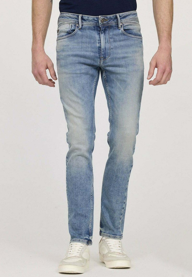 Jean en denim bleu clair avec une coupe ajustée, un design délavé, un style à cinq poches et des coutures contrastées, associés à des baskets blanches.