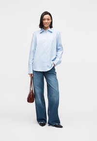 Világoskék ing finom mintával, laza szabású kék farmernadrággal párosítva. Kiegészítők: egy kis barna kézitáska és fekete cipők.