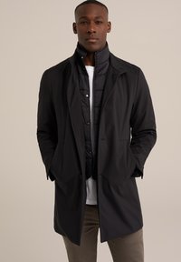 Prenda exterior negra, impermeable, con un diseño estructurado, que cuenta con un cuello alto, cierre con cremallera y botones, y un forro interior acolchado.