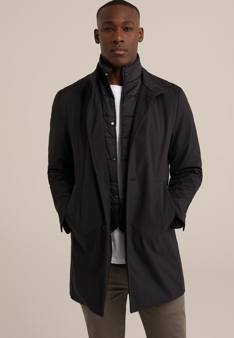 Prenda exterior negra, impermeable, con un diseño estructurado, que cuenta con un cuello alto, cierre con cremallera y botones, y un forro interior acolchado.