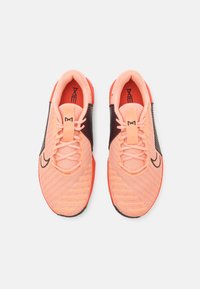 Baskets en mesh corail et noir, avec des accents texturés, bout arrondi et semelle orange contrastante. Lacets et logo sur le dessus.