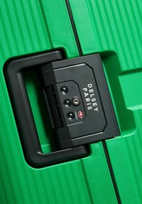 Maleta verde de shell duro con estrías verticales, que presenta un mecanismo de bloqueo negro etiquetado "DELLSEY PARIS" y un diseño aprobado por la TSA.