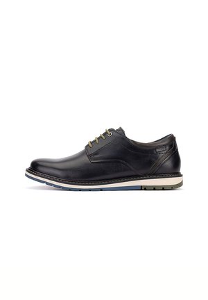 Zapato casual negro de cuero con cordones, suela blanca y azul, tacón bajo y costuras visibles sobre un fondo blanco.