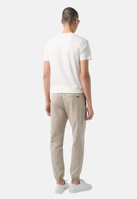 T-shirt blanc à manches courtes associé à un pantalon tapered beige clair et des baskets blanches, avec des poignets élastiques et une poche arrière en accent.