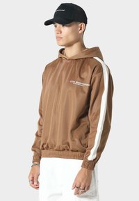 Bruine hooded jas met witte zijstrepen, gemaakt van gladde stof. Voorzien van elastische manchetten en een elastische tailleband, met logo-detail aan de voorkant.