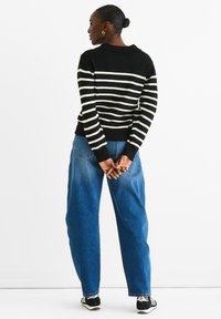 Black and white striped sweater with a round neckline and ribbed cuffs, paired with loose blue jeans and black shoes.