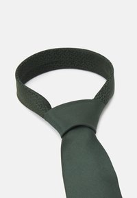 Mørkegrønn slips med teksturert mønster på kragepartiet, glatt stoff på kroppen, med klassisk design og avsmalnet form.