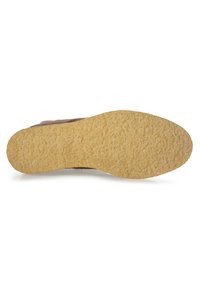 Suela de zapato con una parte inferior de goma amarilla texturizada y un patrón irregular; la parte superior es parcialmente visible en ante marrón.