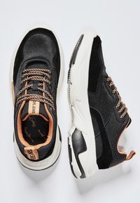 Černé tenisky s kombinací látky a semiše, s kontrastními texturovanými panely, čokoládovými tkaničkami a bílou podrážkou s detaily značky.