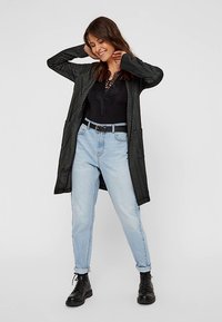 Hosszú, sötétszürke kardigán texturált anyagból, fekete felsővel és világoskék, magas derekú farmerral párosítva. A megjelenést fekete, fűzős csizmák egészítik ki.