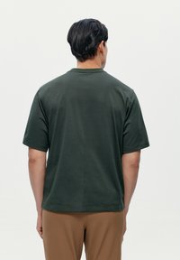 Tmavě zelená polo košile s krátkým rukávem, hladkým povrchem a klasickým límcem, s rovnym lemem a minimalistickými designovými detaily.