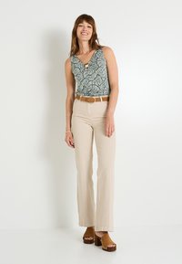 Top sin mangas de estampado floral en verde y blanco, combinado con pantalones acampanados beige. Un cinturón marrón y sandalias de plataforma completan el conjunto.