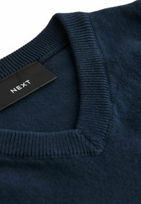 Maglione blu navy a V realizzato in un tessuto morbido. Dettagli a coste sul collo e sull'orlo. Etichetta visibile con il nome del marchio "NEXT."
