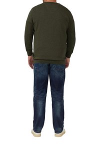Maglione lavorato a maglia verde oliva con maniche lunghe, abbinato a jeans blu strappati e sneakers beidge, visto da dietro.