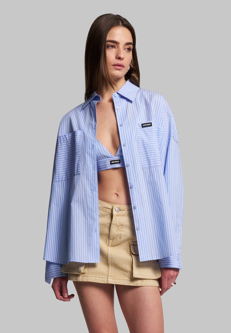 Blue and white striped oversized shirt, button-up design, two front pockets, worn over a matching blue crop top and beige mini skirt.