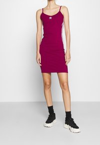Dopasowana magenta sukienka z cienkimi ramiączkami, białymi pasami po bokach i haftowanym logo. Gładki, elastyczny materiał o sylwetce bodycon.