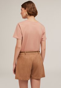 Tricou din bumbac roz deschis cu mâneci scurte, asociat cu pantaloni scurți din suede bej, având o curea asortată. Textură netedă și culori neutre.