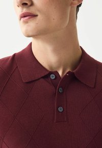Bordo mezgimo polo marškiniai su deimanto raštu, turintys apykaklę ir tris juodas mygtukus. Glotnus audinys ir priderintas dizainas.