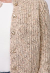 Cárdigan beige de punto con textura acanalada, con botones plateados en forma de concha y sutiles motas de color en toda la tela.