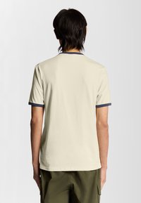 Lys beige t-shirt med korte ærmer, der har en marineblå krave og ærmekanter. Fremstillet af blødt, tekstureret bomuldsstof.