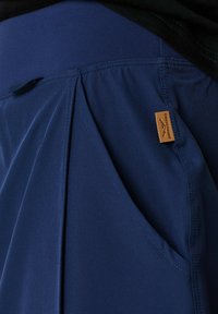 Navy blue lightweight pants with a smooth texture, featuring a pleated design and side pocket, labeled with a small tan tag.