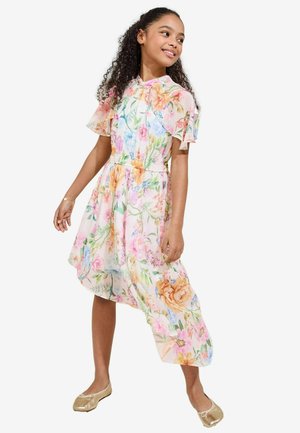 Blumenkleid mit pinken, blauen und orangefarbenen Blumen auf transparenter Baumwolle. Kurze, schwingende Ärmel, elastischer Bund und asymmetrischer Saum. Goldene Ballerinas.