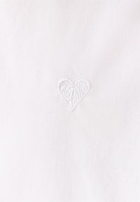 Tela blanca con una textura sutil que presenta un diseño de corazón bordado en hilo blanco a juego.