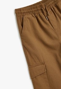 Brune cargo bukser med elastisk talje, justerbar snor, sidelommer og en lomme på låret. Blødt, holdbart stof.